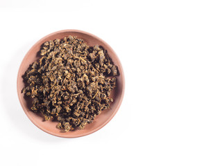 Fermented granular tea from Cherry (Cerasus) leaves on clay plate on white background
