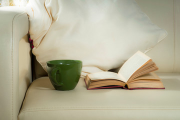 A green mug and a book, on the background of pillows on the bed