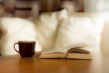 A glass of coffee and a book on the table, on the background of pillows on the bed