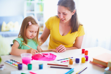 mother daughter paints watercolor on a sheet of paper sitting at home at the table in a bright room.