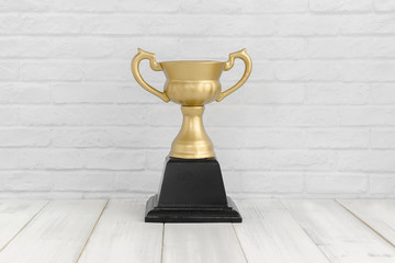 Gold Trophy on white wood table over white brick background with copy space.