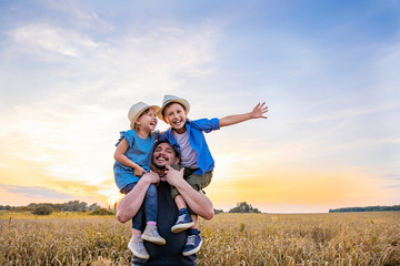 dad holds two children in his arms. happy family playing in the field in the evening sunset.