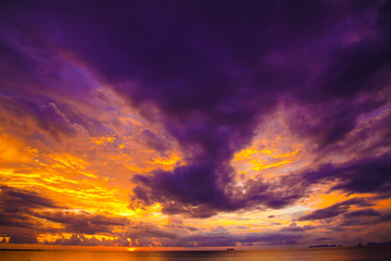 Naklejka na ściany i meble Burning orange, yellow glowing sky and sea during sunset on tropical island after rain and storm with dramatic dark clouds - Ko Lanta, Thailand