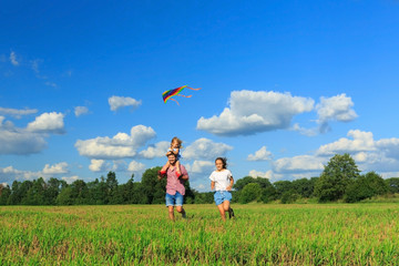 Mother, father and daughter are flying a kite in the field. Front view, copy space.