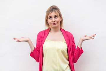 I don't know. Portrait of confused beautiful blond young woman in yellow shirt and red blouse standing, raised arms, confused and thinking. indoor studio shot, isolated on white wall background.