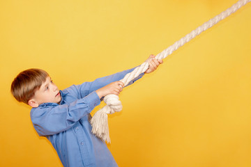 The boy stretches on a rope on a yellow background, the concept of achieving success.
