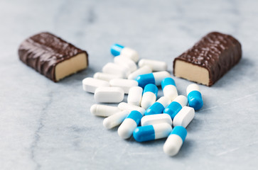 High Protein bar, Tri-Creatine Malate and Arginine capsules and BCAA amino acids.  Bodybuilding food supplements on bright stone background. Close up. 