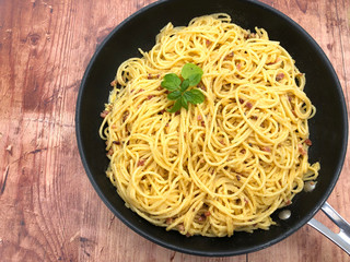 Traditional italian spaghetti carbonara with bacon, eggs, cream and parmesan, cooked in the pan on metallic background.