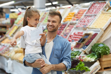 Waist up portrait of smiling father shopping with little girl at farmers market, copy space