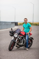 Fototapeta na wymiar Handsome rider man sitting on classic style cafe racer motorbike on highway. Brutal fun urban lifestyle. young man holding bottle, sitting on motorcycle