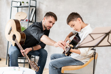 Adult man explains his son, who learn to play guitar, how to play studied chord correctly....