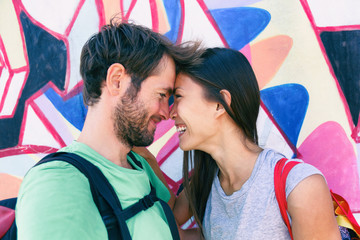 Happy couple in love taking a selfie doing funny kissing pose at famous tourist attraction Berlin wall, Germany, Europe travel destination. Laughing interracial young people tourists.