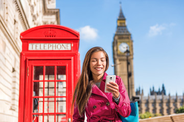 London mobile phone businesswoman walking in the city in stylish pink trench coat, urban lifestyle. Red telephone booth and Big Ben background London, England, UK. Europe travel. - obrazy, fototapety, plakaty