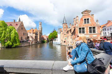 Fototapeta premium A young woman with the flag of Belgium in her hands is enjoying the view of the canals in the historical center of Bruges.
