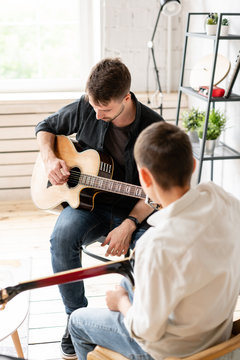 The young teacher shows the correct position of the hands in the guitar on his example