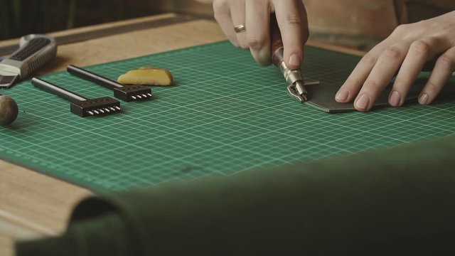 Female skinner draws line for holes by pressing special tool. Master makes wallet in workshop. Handmade leather goods in slow motion