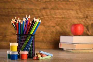 Fototapeta premium School supplies on a warm, beautiful wooden background. Colored children's pencils in a locker black holder for stationery.