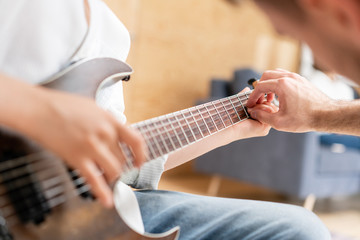 The young teacher helps his student to play electric guitar