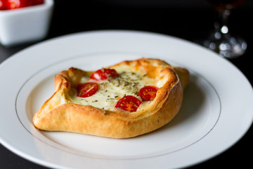 Pizza estillo canoa no elegante prato branco com vinho branco ao fundo e tomates cerejas