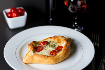 Pizza estillo canoa no elegante prato branco com vinho branco ao fundo e tomates cerejas