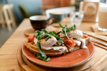 Traditional Belgian waffle with salmon, lettuce leaves and poached egg. A young woman is having Breakfast in a cafe, hands with a fork and a knife close-up.