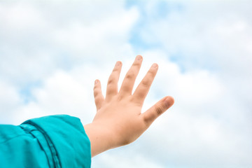 Close up of child hand raised up over blue sky and clouds background. Gesture