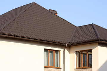 Brown Tiled roof of the house with windows on a background of blue sky