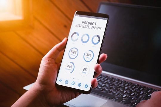 Project management dashboard reports data analytics concept. Close up of young business woman holding smart phone with project management dashboard reports mobile appliaction. 