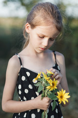 Beautiful, little girl holds in her hands yellow flowers of sunflower.