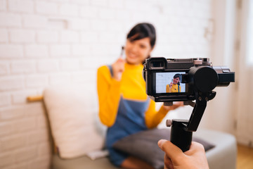 Young Asian woman holding cosmetics brush while recording a video with professional camera. Beauty vlog blogging and internet influencer business concept