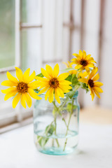 A bouquet of yellow flowers stands in a glass jar on the window.