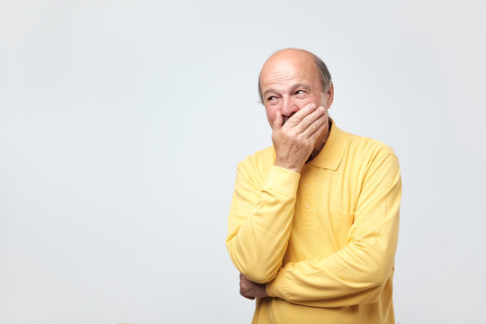 portrait of mature man laughing and covering his mouth with hand over white background. Trying to hold a laugh not to offend some person. He just heard a funny joke