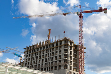 Construction crane and a team of workers are building a multi-storey house against the blue sky with clouds