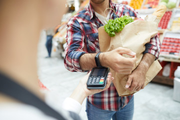 Close up of unrecognizable man paying via smartwatch while grocery shopping at farmers market, copy...