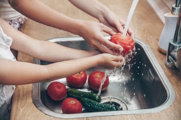 Close up hands of mother and her little daughter cooking salad together and washing vegetables in a...