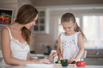 Young mother and her little daughter cooking salad together  in a beautiful white kitchen in Scandinavian-style