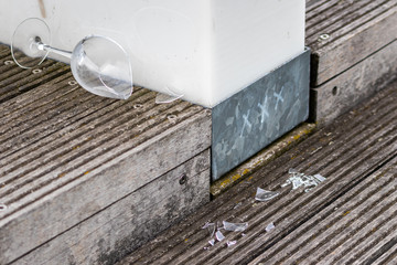 Zerbrochenes Weinglas liegt auf Holzdielen und zeigt die Spuren einer wilden Party mit Alkohol und alkoholisierten Gästen nach der Feier