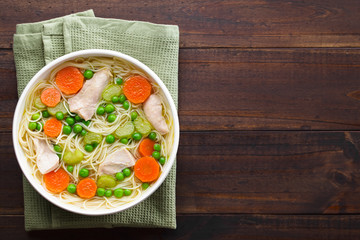 Fresh homemade chicken noodle soup with carrot, peas and celery in white soup bowl, photographed...
