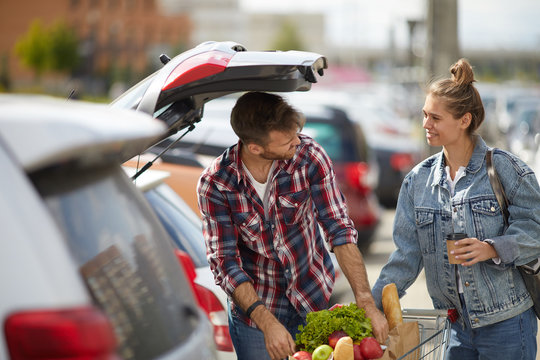 Portrait Of Young Couple Packing Groceries Into Car Trunk Outdoors, Copy Space