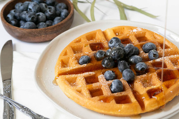 Maple Syrup pouring on Belgian waffle with blueberries, Dusted with Powdered Sugar, White Background, Copy Space