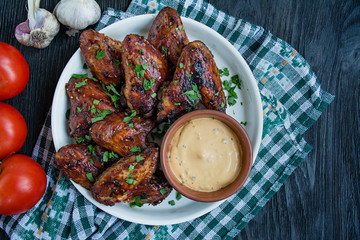 Grilled chicken wings with sauce and herbs.Baked chicken wings in pan. Dark wooden background. Space for text.
