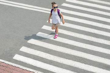 Schoolgirl crossing road on way to school. Zebra traffic walk way in the city. Concept pedestrians passing a crosswalk. Stylish young teen girl walking with backpack. Active child. Top view