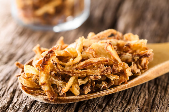 Fresh homemade crispy fried onion strings on wooden spoon (Selective Focus, Focus one third into the image)