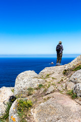 Obraz premium Male pilgrim on the rocks of Cape Finisterre, Cabo Fisterra or Cabo Finisterre - the end of the Way of St. James, Camino de Santiago, Galicia, Spain