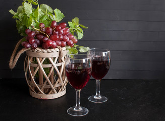 Two glasses of red wine and red grapes on a black wooden table.