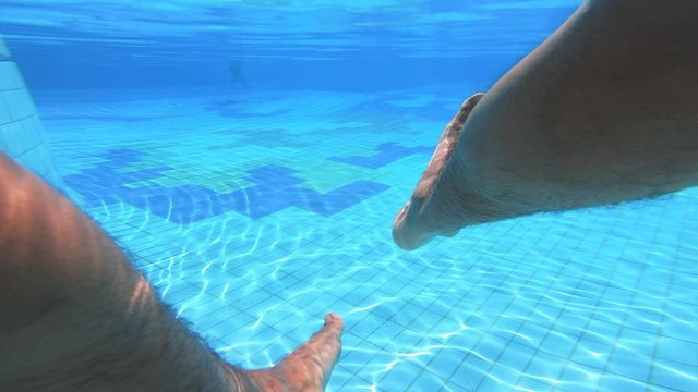 Male legs in the swimming pool are being filmed from underwater