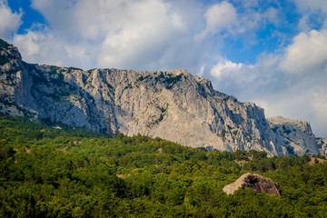Fototapeta premium Russian mountains. Crimea. Summer mountains background. Forest and mountains in the sun on the background of a cloudy sky above the peninsula of Crimea. Sunny, bright, saturated raster photo