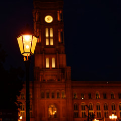 The Red Town Hall in the center of Berlin at night. In the foreground is a historic Berlin lantern on which the focus lies. The town hall is out of focus in the background.