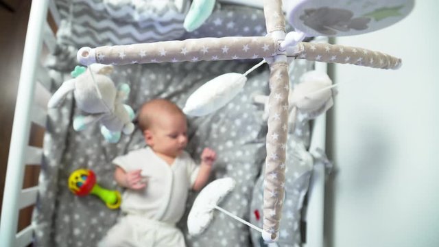 Baby bay  on a child bed looking at spinning mobile toy. 4K.