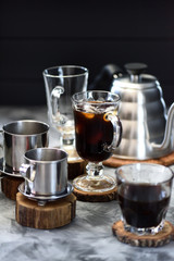 Vietnamese black drip ice coffee in irish mug with phin and gooseneck kettle on black background